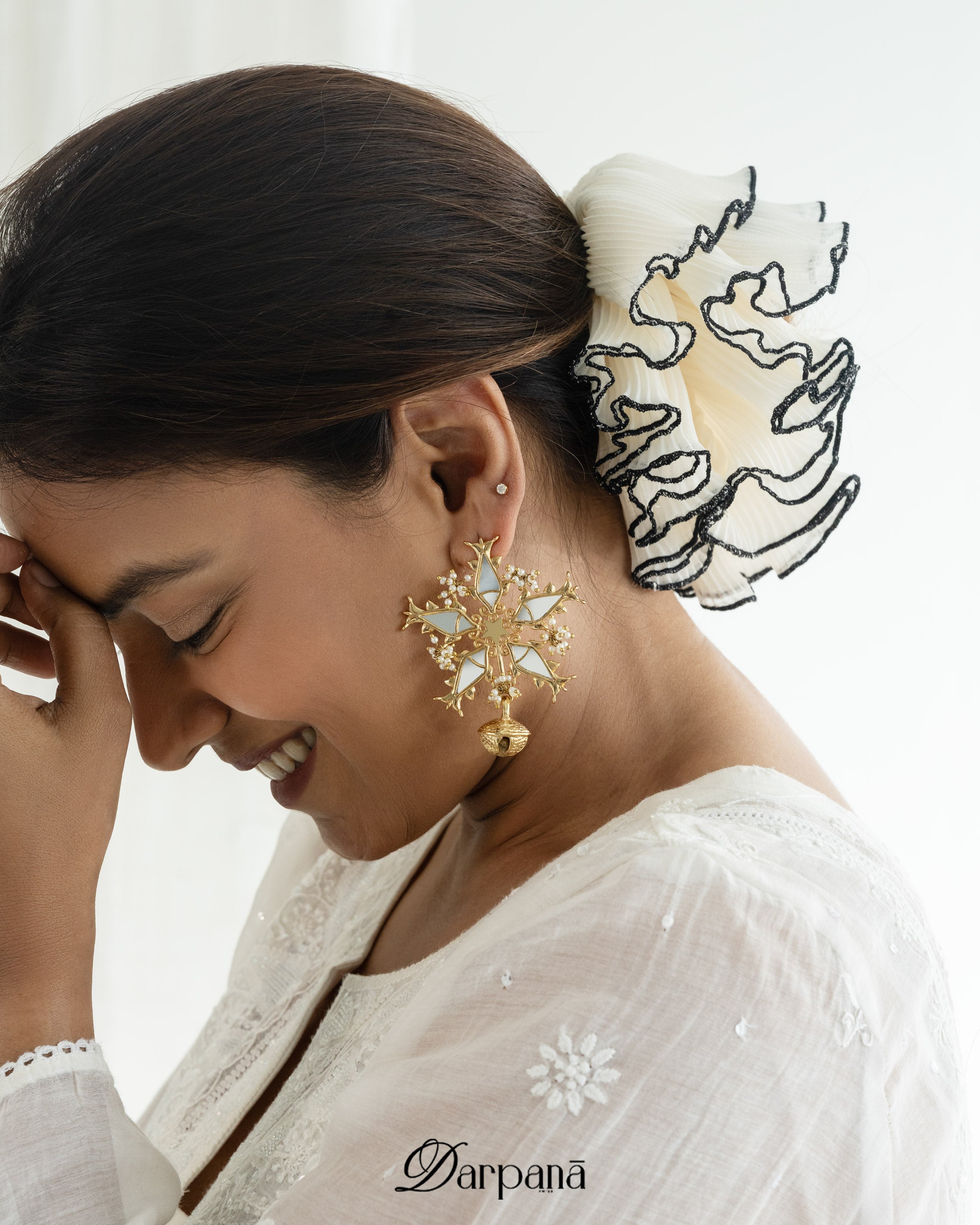 Woman wearing gold earrings with a white blouse, 'Darpana' brand visible