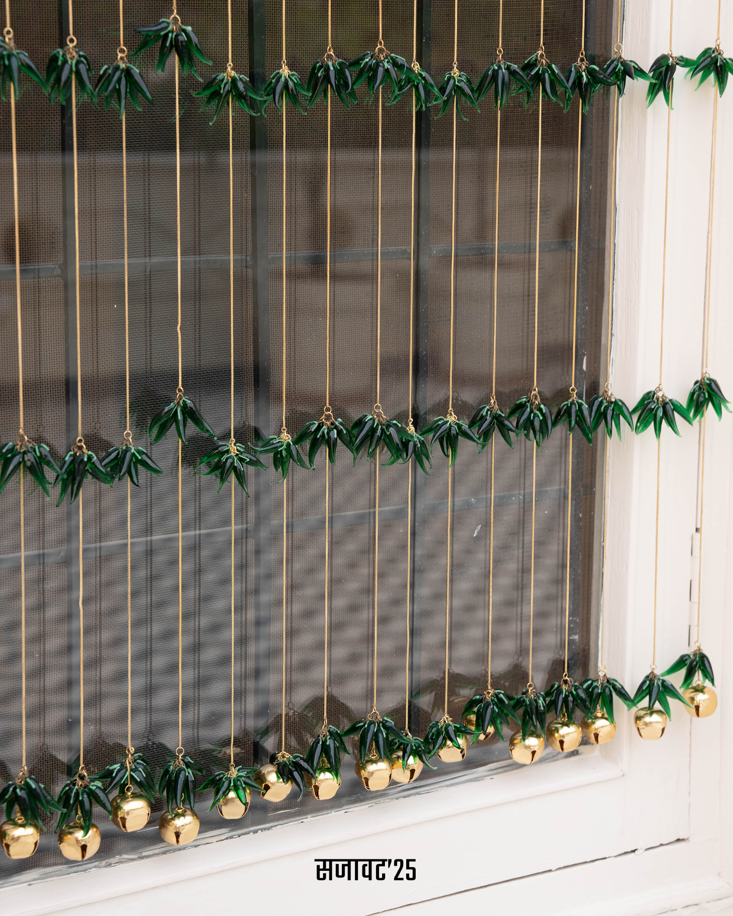 Decorative string with green leaves and gold balls hanging against a window.