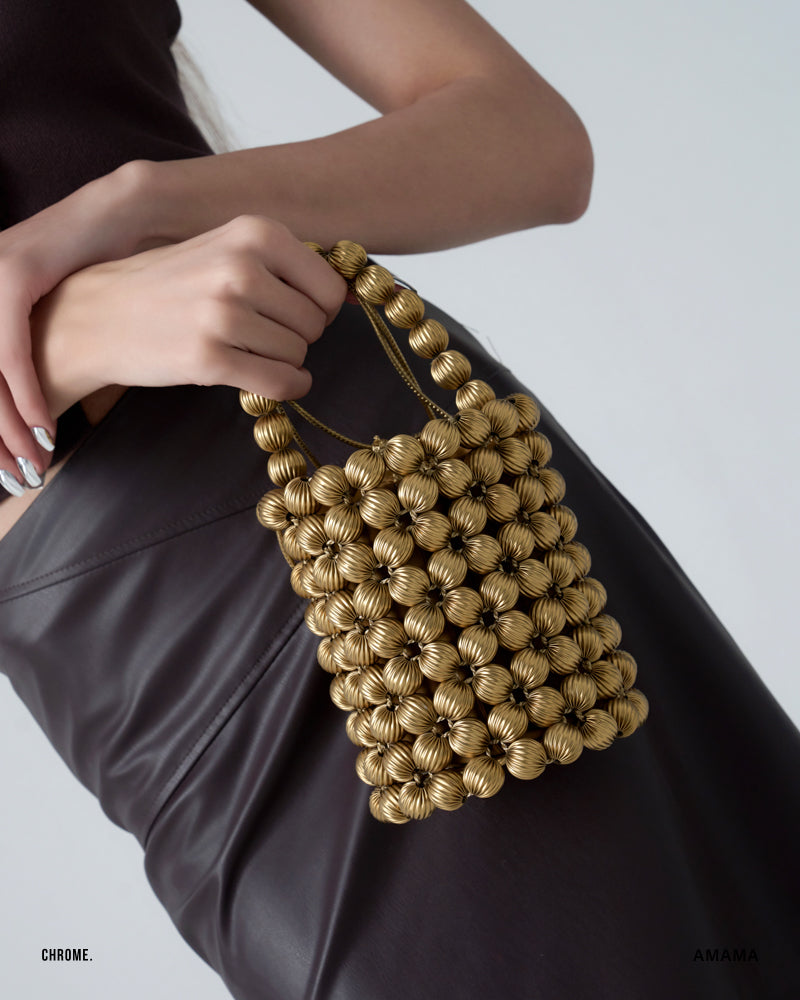A person holding a bucket bag with a light gold color made of woven beads.