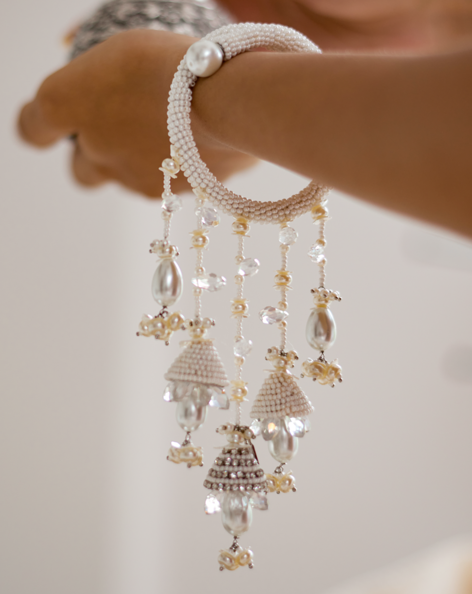 A hand holding a white conoidal rose lumba accessory with intricate details and small bell-like adornments.