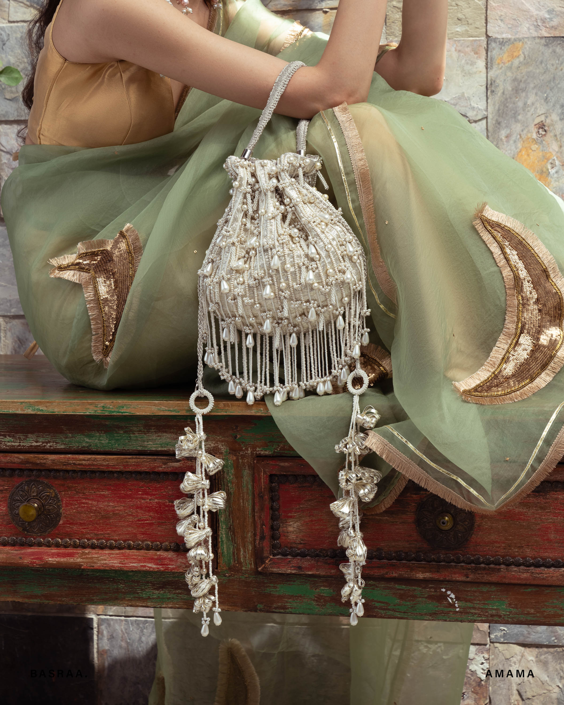Decorative handbag with intricate design held by a person wearing a green saree.