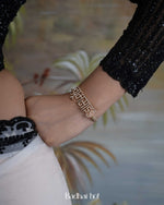 Close-up of a wrist wearing a gold bracelet with text, against a blurred indoor background.