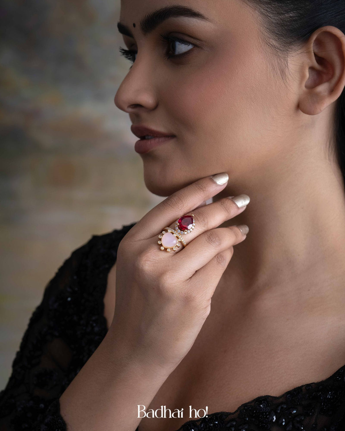 Woman wearing a ring with a prominent gemstone, against a blurred background.

