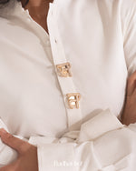 Close-up of a white garment with gold buckles, featuring the brand ''.

