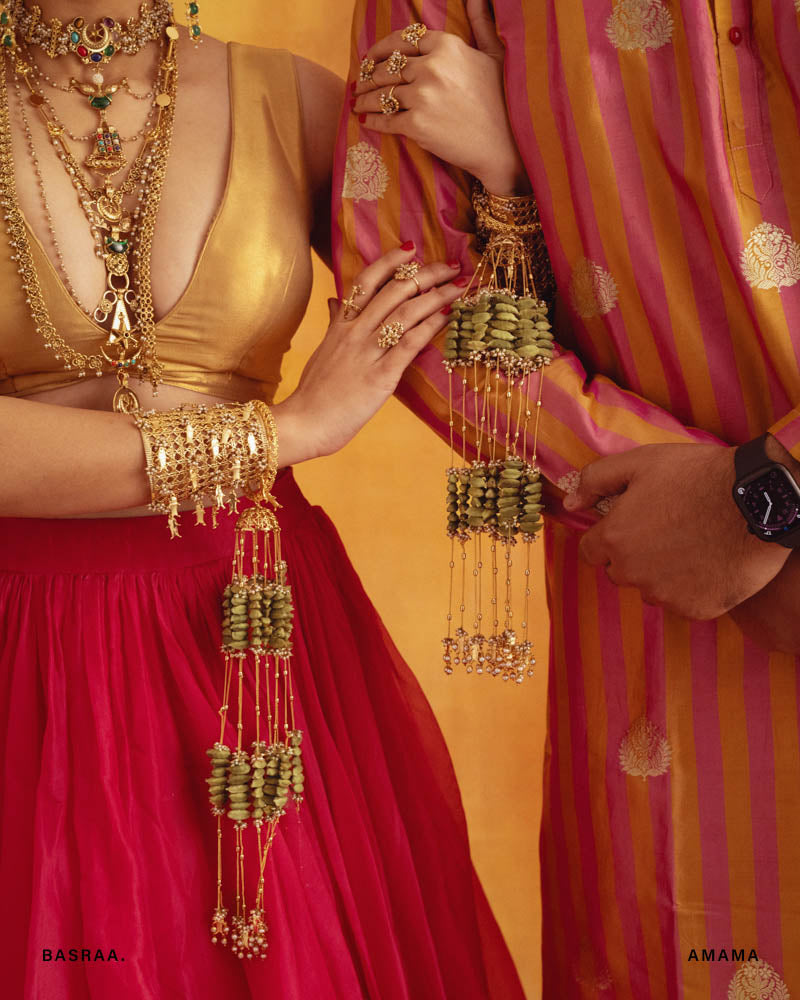 A close-up of traditional Afghani jewelry, featuring gold-colored metalwork and multicolored gemstones, worn by a person dressed in a red and pink traditional outfit.