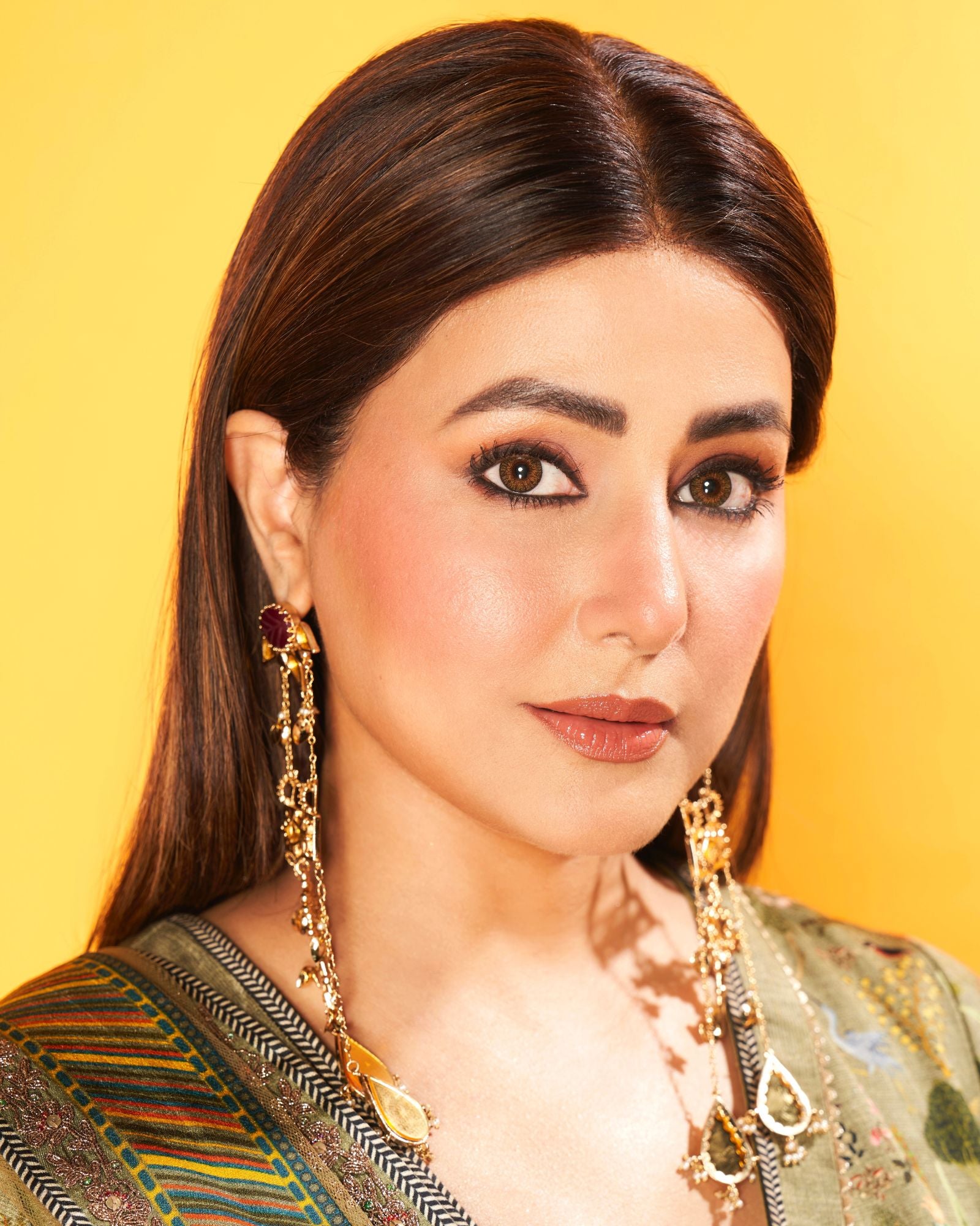 Woman wearing gold earrings with a yellow background

