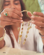 Gold rakhi lumba being held by a hand against a beige background, with 'DOR' and 'AMAMA' branding visible.