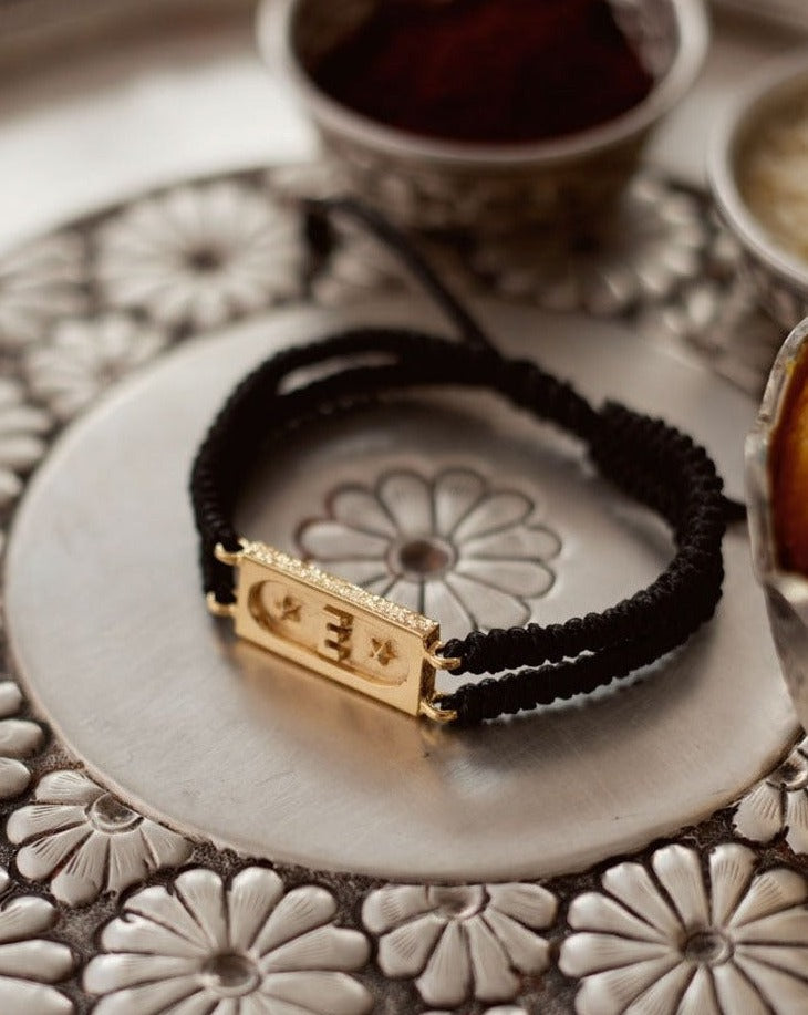 A jet black bracelet with a gold-tone brick bond design, displayed on a silver plate with floral patterns in the background.